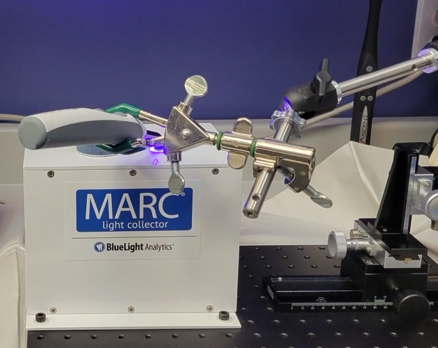 The MARC-LC on a laboratory bench, with a curing light held in its top measurement port by an articulated arm.