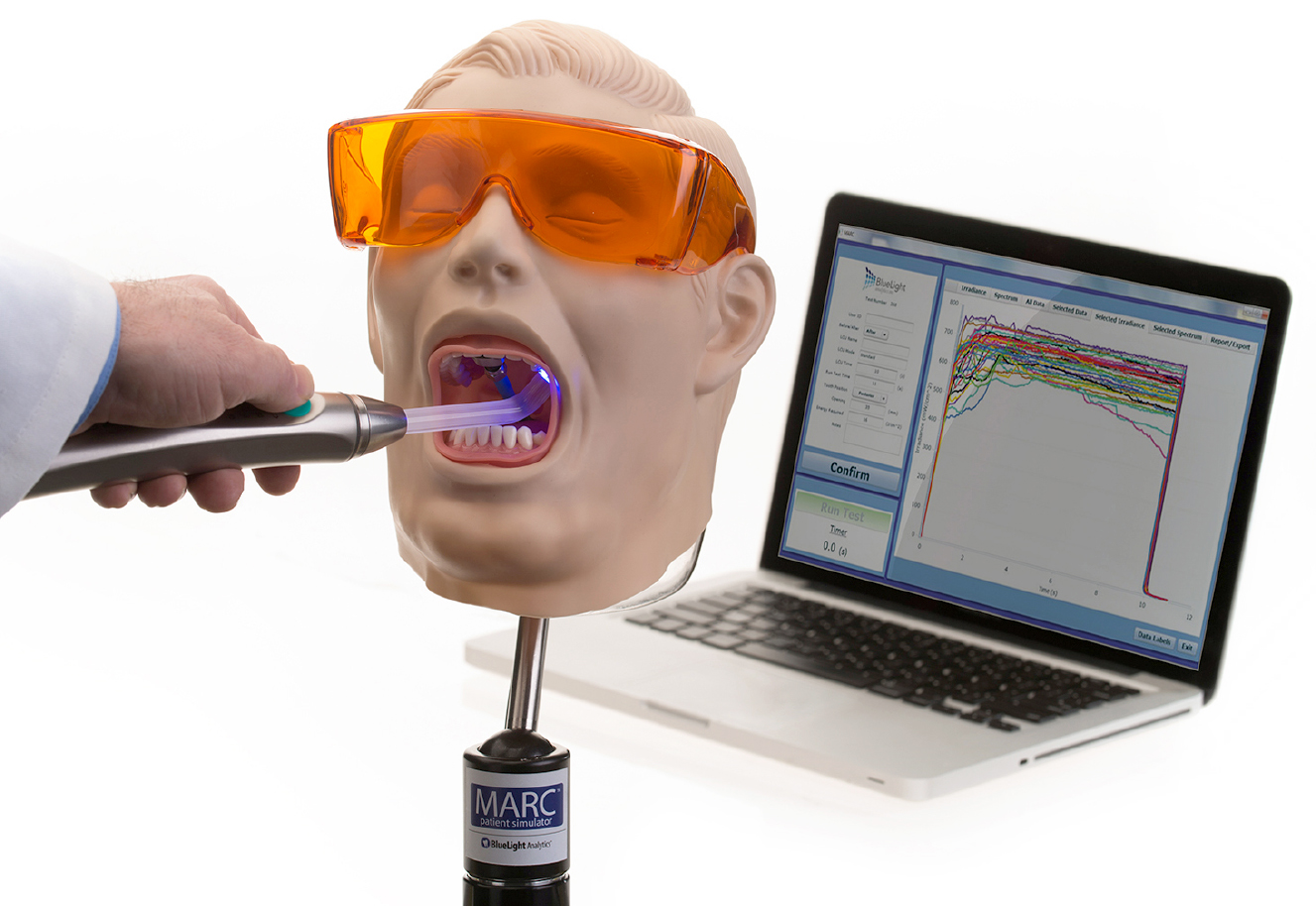 The MARC Patient Simulator: a manikin head being light-cured while the software plots live irradiance and spectral data on a laptop.